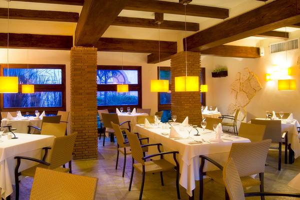 Innenansicht des Restaurants im IFA Villas Bavaro Hotel mit Tisch und Stühlen, hängenden Lampen und Fenstern.