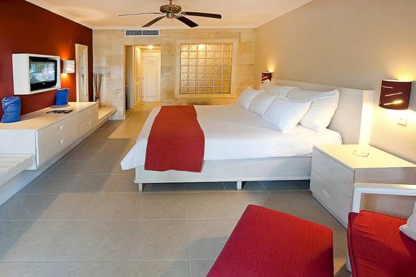 Schlafzimmer im IFA Villas Bavaro Hotel mit einem großen Bett, roter Decke, weißen Kissen und modernen Möbeln.