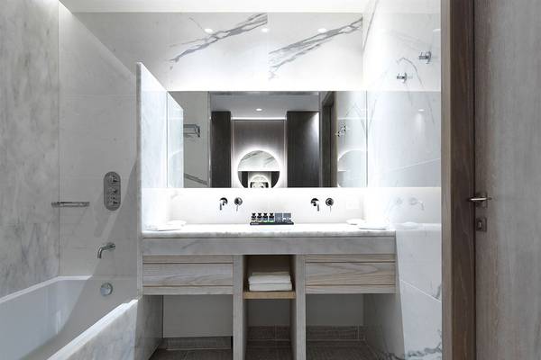 Ein modernes Badezimmer mit weißen Marmorwänden und Boden, einer Badewanne und einem Doppelwaschbecken mit Holzschubladen.