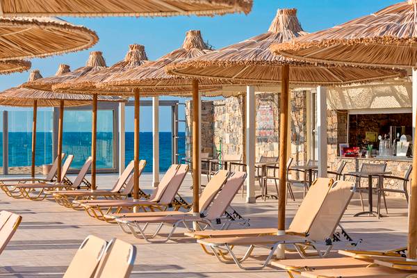 Lounge-Bereich im Freien des Civitel Creta Beach Hotels mit Sonnenliegen und Strohschirmen am Meer.
