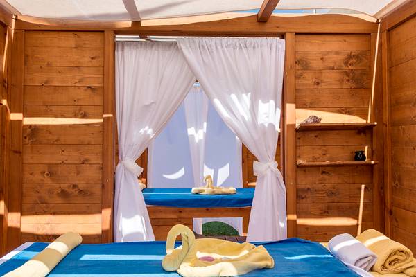 Massageraum im Civitel Creta Beach Hotel mit Holzwänden, weißen Vorhängen und blauen Liegen.