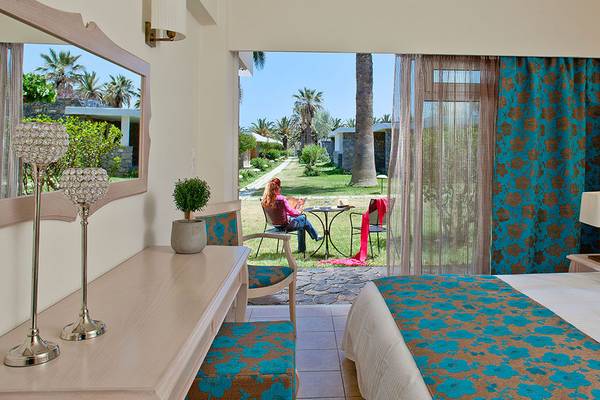 Innenansicht eines Zimmers im Civitel Creta Beach Hotel mit Blick auf eine Frau, die auf einer Terrasse sitzt.