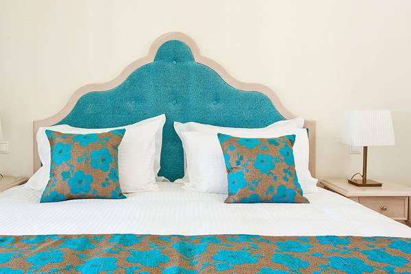 Hotelbett mit blauem Kopfteil und blau-braunen Kissen, weiße Kissen, zwei Lampen auf Nachttischen