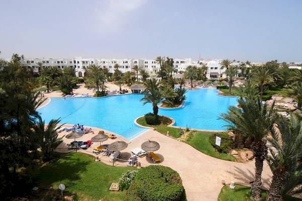 Luftaufnahme des großen Swimmingpools des Djerba Resorts mit umliegenden Liegestühlen und Palmen.