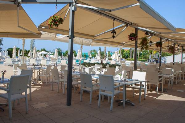 Restaurant-Terrasse des Louis Imperial Beach Hotels mit vielen Tischen und Stühlen unter Sonnenschirmen.
