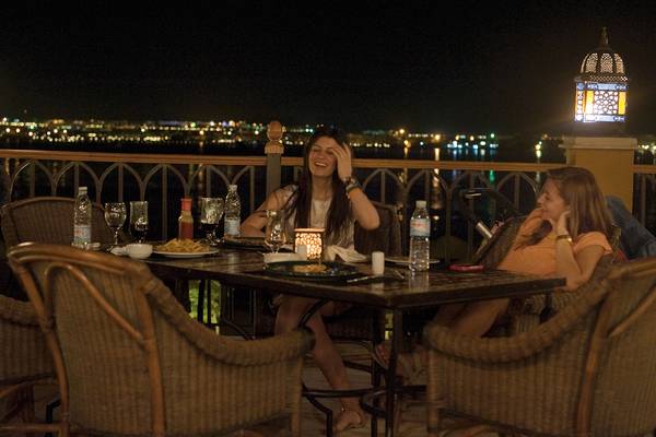 Zwei Frauen sitzen auf einer Terrasse bei Nacht und lachen.