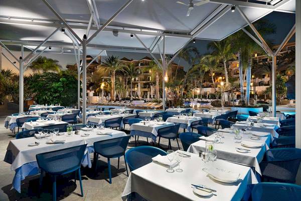 Abendliche Außenterrasse des Jardines de Nivaria Hotels mit blauen Stühlen und Tischen, umgeben von Palmen und Gebäuden.