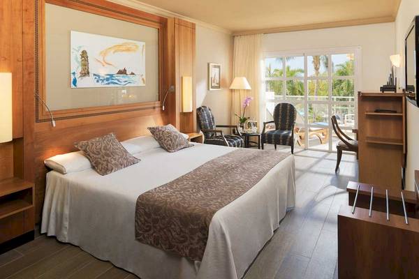 Innenansicht eines Schlafzimmers im Jardines de Nivaria Hotel mit Doppelbett, Sitzbereich und Balkonzugang.