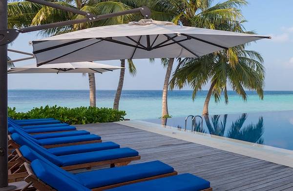 Pool-Deck des Noku Maldives mit blauen Liegestühlen und weißen Sonnenschirmen am Meer