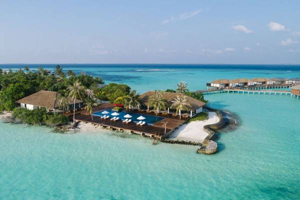 Luftaufnahme des Noku Maldives Resorts mit Pool, Loungeliegen und Steg zum Meer