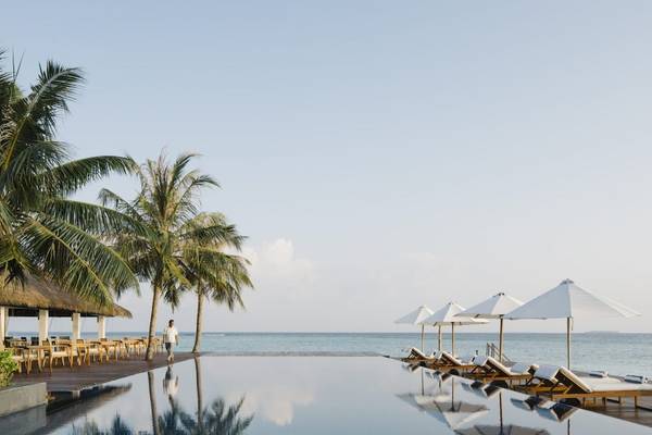 Außenpool des Noku Maldives mit Loungeliegen und Sonnenschirmen am Strand