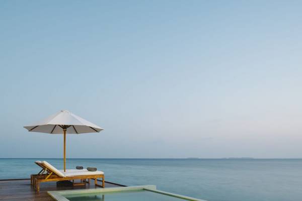 Strandliegestuhl mit Schirm am Pool des Noku Maldives Hotels