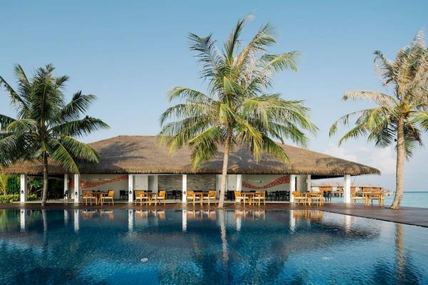 Außenbereich des Noku Maldives Hotels mit Swimmingpool, Tischen und Stühlen.