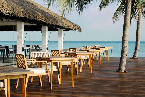 Außenterrasse des Noku Maldives Hotels mit Holztischen und Stühlen, Blick aufs Meer.