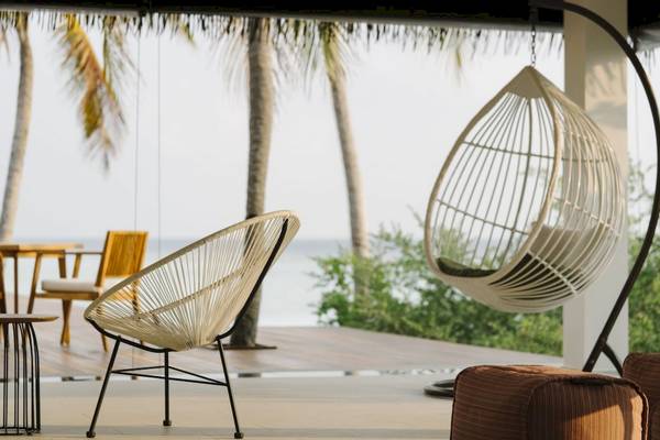 Terrasse des Noku Maldives Hotels mit einem Korbstuhl, einem Stuhl und einem Tisch vor einem Meerblick.