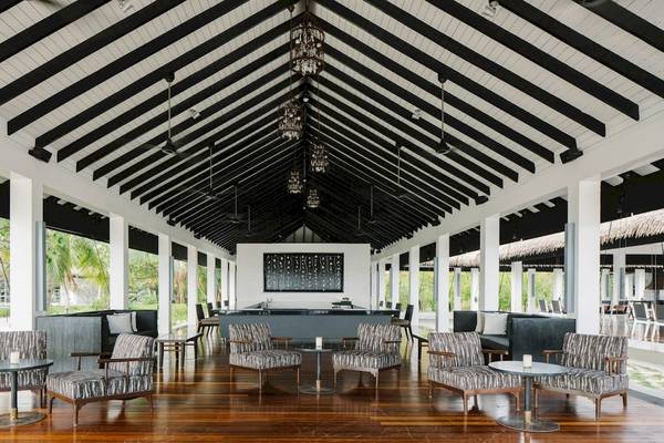 Loungebereich des Noku Maldives Hotels mit schwarzen und weißen Möbeln und Holzboden.