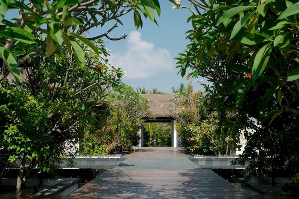 Eingang des Noku Maldives Hotels umgeben von tropischen Pflanzen und Bäumen.