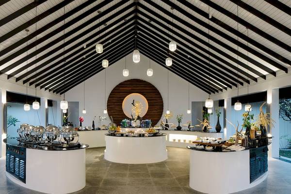 Innenansicht des Restaurants im Noku Maldives mit runden Tischen und hängenden Lampen.