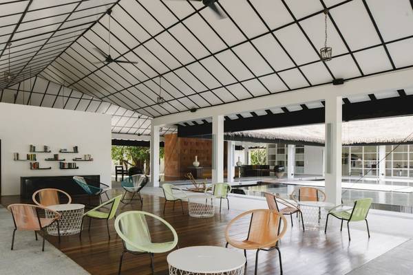 Loungebereich im Noku Maldives Hotel mit bunten Stühlen und Tischen auf einem Holzboden.