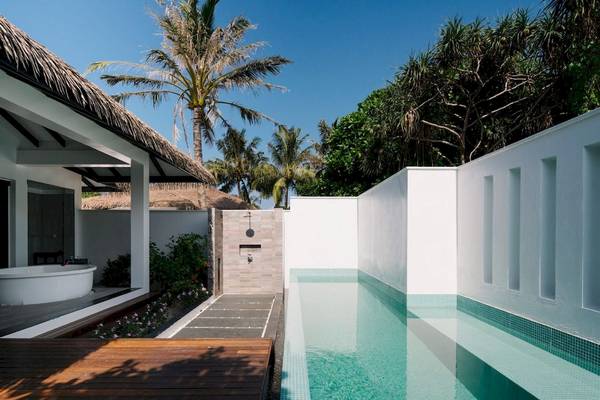 Außenpool und Badewanne im Noku Maldives Hotel, umgeben von Palmen und Pflanzen.