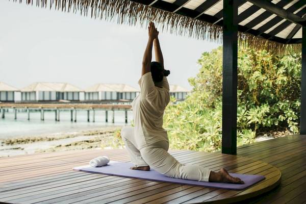 Frau macht Yoga auf einem Holzdeck im Noku Maldives.
