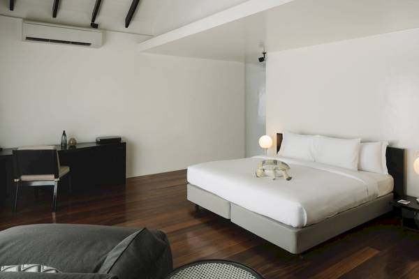 Innenansicht eines Schlafzimmers im Noku Maldives Hotel mit einem Bett, Nachttischen und Schreibtisch.