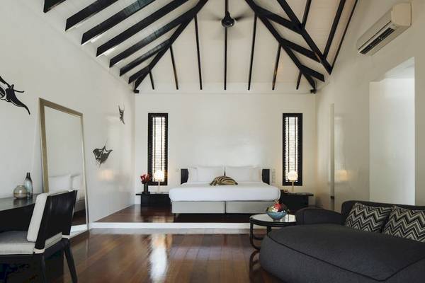 Innenansicht eines Schlafzimmers im Noku Maldives Hotel mit Bett, Sofa, Schreibtisch und Lampe.