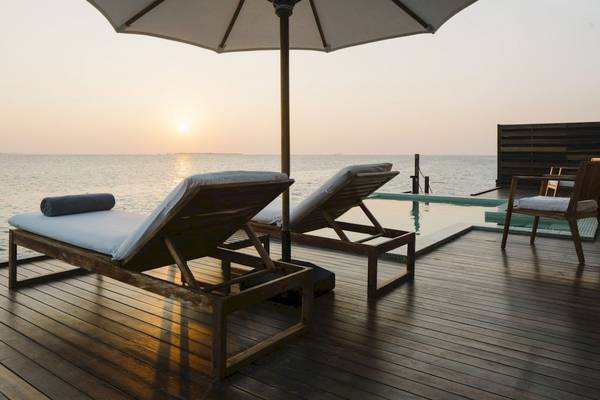 Zwei Holzliegen mit einem Pool am Abend unter einem Sonnenschirm am Noku Maldives