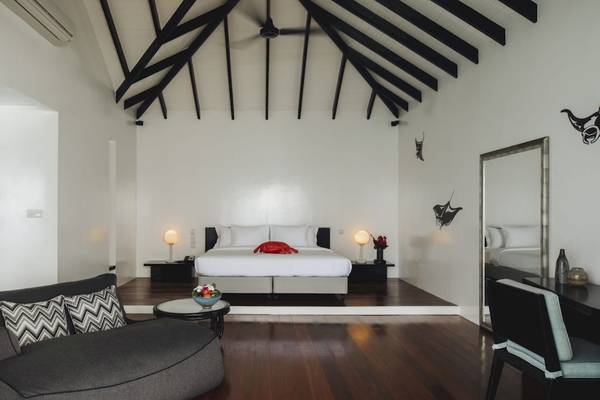 Schlafzimmer im Noku Maldives Hotel mit hohem Dach, weißen Wänden und Holzboden.