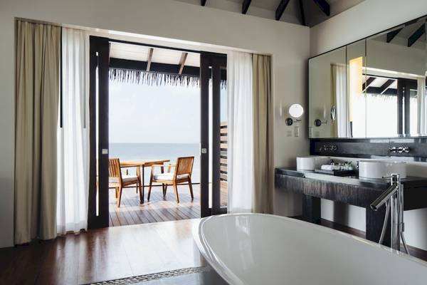 Badezimmer im Noku Maldives mit Blick auf das Meer und eine Terrasse mit Tisch und Stühlen.