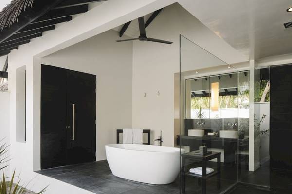Badezimmer im Noku Maldives Hotel mit Badewanne, Glasdusche und schwarzen Türen.
