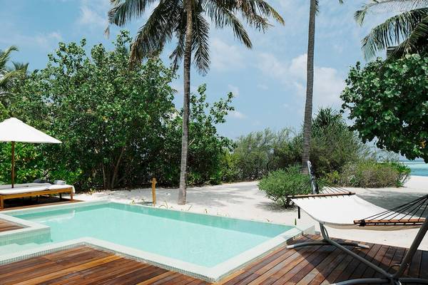 Außenpoolbereich des Noku Maldives Hotels mit Loungebetten und Sonnenschirm.
