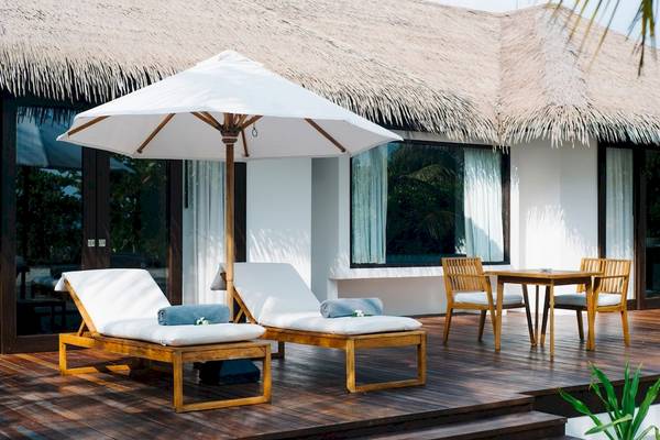 Terrasse im Noku Maldives mit Sonnenliegen, Tisch, Stühlen und einem Sonnenschirm