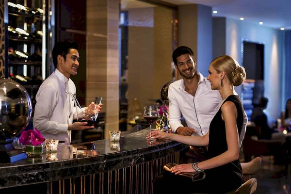 Ein Mitarbeiter serviert Getränke an der Bar im Sofitel Bangkok Sukhumvit an zwei Kunden.