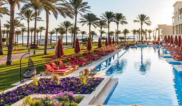 Außenbereich des Rixos Premium Seagate Hotels mit einem langen Pool, roten Liegestühlen und Palmen
