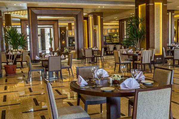 Innenbereich des Restaurants im Rixos Premium Seagate Hotel mit runden Tischen und Stühlen, illuminierten Säulen und Pflanzen.