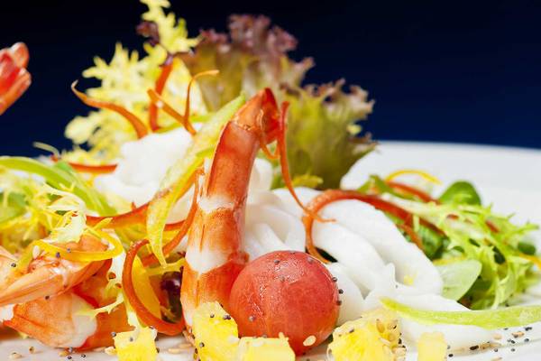 Nahaufnahme von Garnelen und Salat auf einem weißen Teller mit einer blauen Hintergrund.