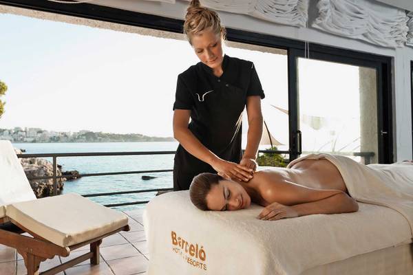 Frau mit Massagetuch liegt auf dem Rücken, massiert von einer Therapeutin mit Blick auf das Meer.