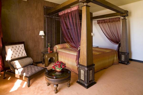 Luxuriöses Schlafzimmer im Royal Atlas & Spa Hotel mit Baldachinbett, Nachttischen und einem Blumenstrauß.