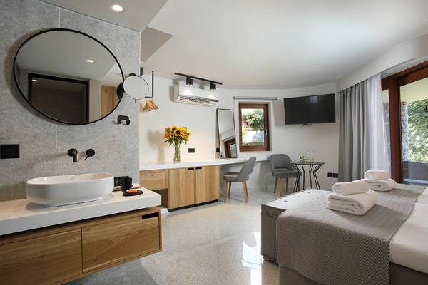 Innenansicht eines Hotelzimmers mit Badezimmer und Schlafbereich, inklusive Bett, Schreibtisch und Fernseher.