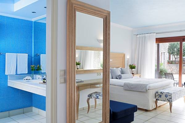 Ein Schlafzimmer im Ikaros Beach Luxury Resort & Spa mit heller Einrichtung, einem großen Bett, und einem Badezimmer mit blauen Fliesen.