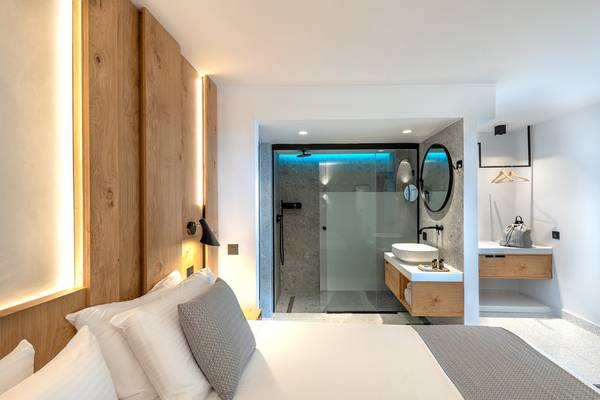 Innenansicht eines Zimmers im Ikaros Beach Luxury Resort & Spa mit Bett, Badezimmer und Holzelementen.
