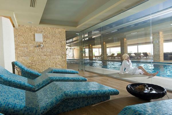 Ein Innenpool im Ikaros Beach Luxury Resort & Spa mit einer Frau in einem weißen Bademantel, die sich entspannt.