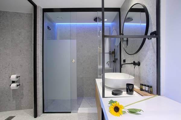 Badezimmer im Ikaros Beach Luxury Resort & Spa mit Glasdusche, Waschbecken und Sonnenblume.