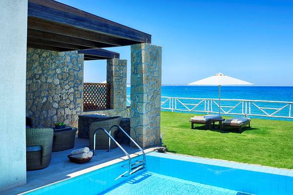 Poolbereich des Ikaros Beach Luxury Resort & Spa mit Loungemöbeln und Blick auf das Meer.
