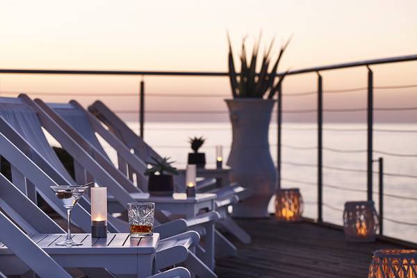 Abendliche Terrasse im Ikaros Beach Luxury Resort & Spa mit weißen Liegen, Pflanzen und Meerblick.