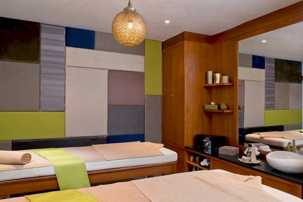 Massageraum im Sofitel Agadir Royal Bay Resort mit zwei Massagetischen, farbigen Wandverkleidungen und einer Lampe.