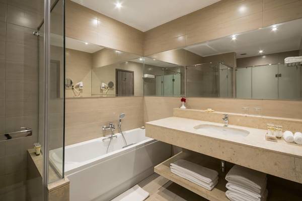 Ein modernes Badezimmer mit Badewanne, Waschbecken und Spiegeln im Steigenberger Alcazar Hotel.