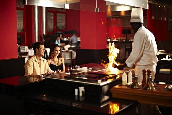 Ein Paar genießt das Essen im Restaurant des Iberostar Grand Rose Hall Hotels, während der Koch am Tisch Feuer macht.