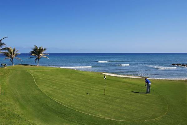 Golfplatz am Strand mit Blick auf das Meer und Palmen, Spieler in Blau.